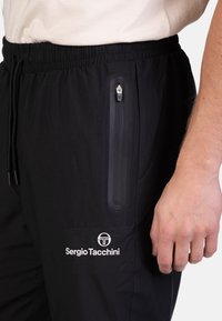 Zwarte sportbroek met een elastische tailleband, een ritszak en een merklogo. Het materiaal lijkt glad met een matte afwerking.