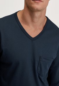 Marineblauwe V-hals, lange mouwen shirt van zachte stof, met een borstzak aan de linkerkant en een gladde textuur.