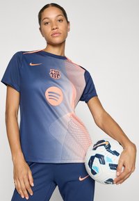 Navy sports t-shirt with orange accents and a Barcelona logo, featuring a wavy pattern. Paired with navy pants and a soccer ball.