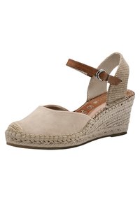 Beige mokasini kenkä, jossa on punottu jute-pohja. Nilkkahihna ruskealla korostuksella ja avoin varvasmuotoilu. Teksturoitu sivupaneeli.