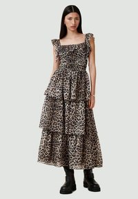 Leopardo rašto maksi suknelė su raukiniais petnešomis, smulkinta liemeniu ir sluoksniuotais sluoksniais. Dėvima su juodais masyviu batais. Pusiau skaidri medžiaga.