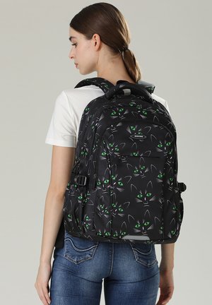 Schwarzer Rucksack mit einem Katzenkopfmuster und grünen Augen, aus strapazierfähigem Material gefertigt, mit gepolsterten Tragegurten und mehreren Fächern ausgestattet.