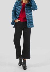 Polstret turkis jakke, rød sweater og mørk denim jeans med vidde. Sorte ankelstøvler. Glat stof med quiltedetalje på jakken.