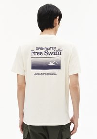 Crème-kleurig katoenen T-shirt met een grafische print op de achterkant met de tekst "OPEN WATER Free Swim" en een zwemillustratie in donkerblauw.