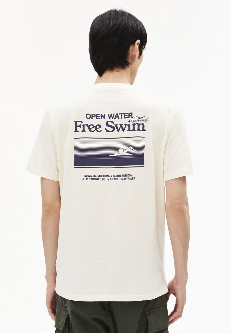 Crème-kleurig katoenen T-shirt met een grafische print op de achterkant met de tekst "OPEN WATER Free Swim" en een zwemillustratie in donkerblauw.