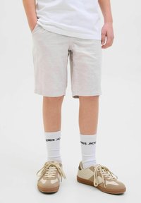 Ljusgrå shorts med en strukturerad yta, kombinerat med beiga sneakers och vita strumpor med svart text. Outfit har en avslappnad stil.