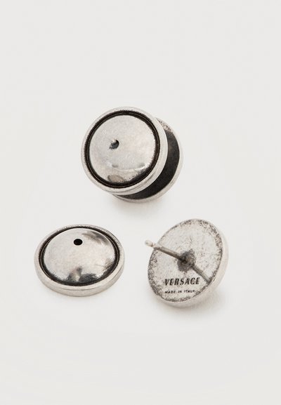 Τρία στρογγυλά ασημένια σκουλαρίκια με λίγο κυρτή επιφάνεια, το ένα δείχνει "VERSACE MADE IN ITALY" στην πίσω πλευρά.