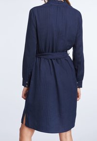 Granatowa sukienka koszulowa z długimi rękawami, teksturowana tkanina, pasek w talii oraz boczne rozcięcia. Guziki przy mankietach.