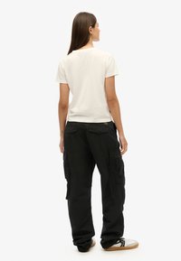Witte katoenen t-shirt, korte mouwen, gecombineerd met zwarte cargo-broek met meerdere zakken, ruime pasvorm en gestructureerde stof. Casual sneakers.