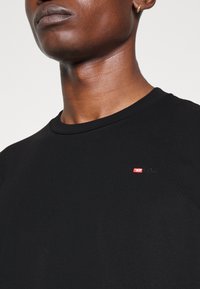 T-shirt in cotone nero con colletto a girocollo e un piccolo logo Diesel ricamato sul petto. Texture liscia con una forma aderente.