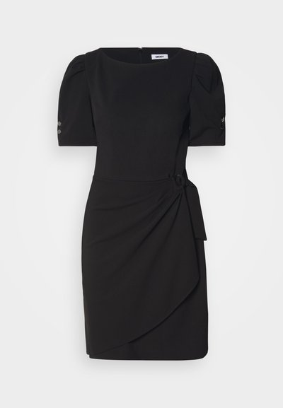 Robe noire avec des manches bouffantes, un col rond, un détail de nœud sur le côté et une jupe drapée asymétrique. Fabriquée en tissu lisse avec une fermeture éclair.