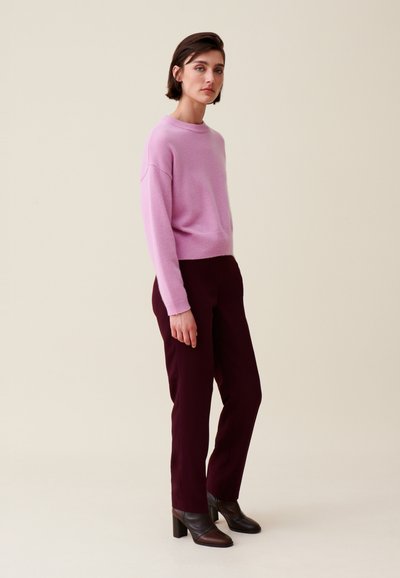 Pull en cachemire rose clair avec un col rond et des épaules tombantes, associé à un pantalon ajusté bordeaux foncé et des bottines à talons marron.