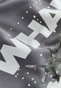 Grauer Stoff mit großem weißen Text und Design eines sternenübersäten Hintergrunds sowie abstrakten Formen. Die Textur wirkt glatt und leicht reflektierend.