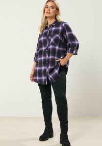 Liila ruudullinen nappipaita rentoon istuvuuteen, jossa on kolmannespituiset hihat, yksi rintatasku ja kaareva helma. Yhdistetty mustiin farkkuihin.