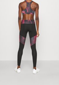 Černé sportovní legíny s růžovým abstraktním vzorem a síťovanými doplňky, doplněné odpovídající sportovní podprsenkou; obojí má přiléhavý střih.