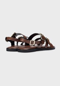 Sandalias de cuero marrón con múltiples correas entrelazadas y hebillas en tono dorado. Suela plana con una textura suave, diseño minimalista.