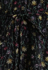 Czarna sukienka w kwiaty z teksturowanej tkaniny z kolorowymi wzorami kwiatowymi w odcieniach żółtego, różowego i białego. Zawiera guziki i związany w talii pas.