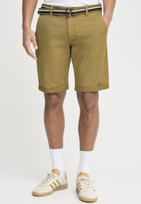 Pantaloni scurți din bumbac khaki cu manșete rulotate, având un curea cu dungi alb-negru. Purtați cu șosete albe și adidași bej.