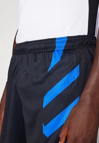 Shorts de sport noirs avec des rayures en chevron bleues, une taille élastique et un tissu texturé, conçus pour le confort et la mobilité.