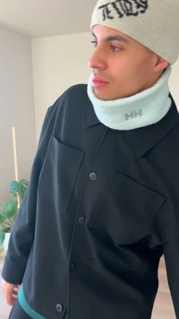 Juoda marškinėliai su didelėmis kišenėmis ir kontrastiniu turkio spalvos apvadu, derinami su šviesiai mėlynu kailiniu kaklo šildytuvu su logotipu.