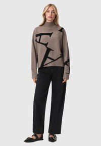 Maglione grigio a maglia con motivi lettera neri, colletto alto e polsini a coste, abbinato a pantaloni in denim neri a gamba larga e scarpe flat nere.