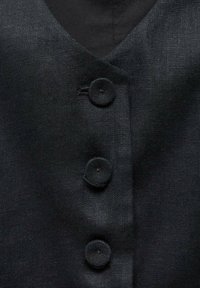 Tissu noir texturé avec trois boutons mats espacés uniformément en ligne verticale sur le devant d'un vêtement.