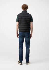 Sort puffer vest med høj krave, der har en quiltet design. Kombineret med blå denimjeans og sko i neutrale nuancer.