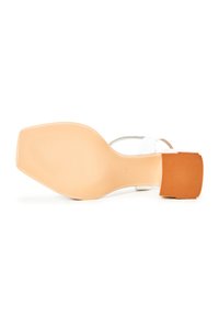 Sandale albe cu vârful pătrat, talpă texturată bej și un toc mic din bloc maro. Prezintă o curea transparentă și un design minimalist.