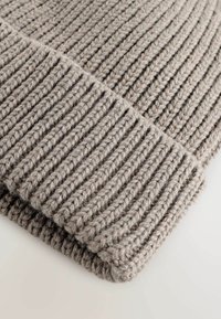 Lysegrå strikket hue med ribbet tekstur, der har brede linjer og en foldet kant. Fremstillet af tyk, blød garn for varme.