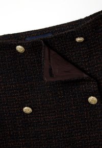 Chaqueta de tweed marrón oscuro con una superficie texturizada, que presenta botones dorados y un forro liso visible en el cuello.