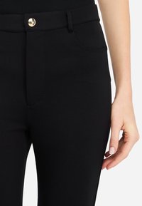 Pantalons stretch noirs avec une silouhette ajustée, comprenant une fermeture à bouton doré, des poches avant et une texture lisse.