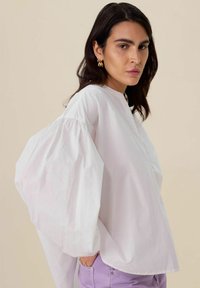 Witte blouse met lange mouwen, puffmouwen en een ronde hals. Gemaakt van lichtgewicht, textuurstof. Gecombineerd met lavendelkleurige broek.