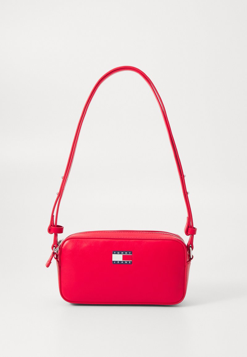 Czerwona skórzana torebka crossbody o prostokątnym kształcie, z metalową plakietką z logo, zamknięciem na zamek błyskawiczny oraz regulowanym paskiem na ramię.