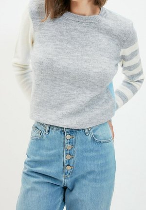 Grijze gebreide trui met contrasterende gestreepte mouwen; gecombineerd met hoge blauwe denim jeans met knoopsluiting en een vervaagde textuur.