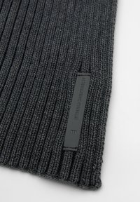 Sciarpa a maglia rigata di colore grigio scuro con un tessuto texturizzato. Presenta un'etichetta in pelle nera con la scritta "ALTERNATIVE CULTURE" in rilievo. Orientamento disteso.