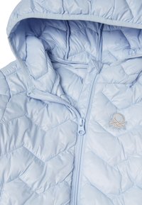 Světle modrá péřová bunda s prošívaným vzorem, předním zipem a malým vyšívaným logem chobotnice na hrudi.