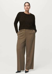 Suéter de leopardo marrón combinado con pantalones de pierna ancha beige y tacones de punta negra, de pie contra un fondo neutro.