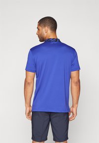 Polo majica s kratkimi rokavi v modri barvi z ovratnikom v črno-modrem vzorcu, izdelana iz gladkega blaga, prikazana na moškem figurativno od zadaj.