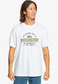 White cotton t-shirt with short sleeves, featuring a black and yellow graphic text reading "Quiksilver." Straight hem and relaxed fit.