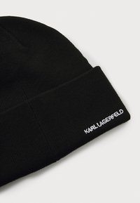 Gorro negro de punto con diseño de vuelta y texto bordado en blanco que dice "KARL LAGERFELD" en el lateral. Textura suave.