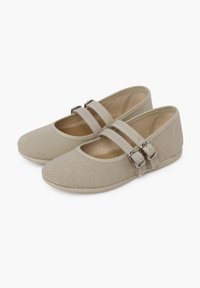 Chaussures en tissu beige avec une finition texturée, bout arrondi et deux sangles ajustables avec des boucles en argent. Semelle plate et design simple.