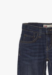 Jeans de mezclilla de color azul marino con un ajuste slim, que cuentan con una cremallera, bolsillos frontales y costuras doradas en contraste. Etiqueta de Levi's en la cintura.