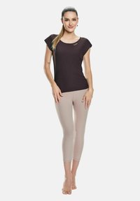 Top scurt de culoare violet închis, cu decolteu rotund și logo auriu, purtat cu colanți bej deschis până la gleznă. Modelul stă desculț.