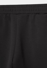 Detailný záber čiernej látky s elastickým pásom a viditeľným detailom švu na mäkkom textúrovanom materiáli.