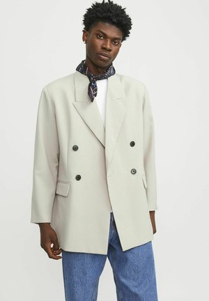 Světle šedý dvouřadý blazer s širokými klopami, černými knoflíky a bočními kapsami. Nosit na bílé košili a doplněný modrými džínami.