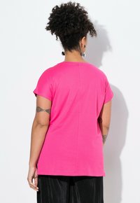 Fuchsiové tričko s krátkým rukávem vyrobené z měkké tkaniny, s kulatým výstřihem a rovným střihem. Na zadní straně je vertikální šev.