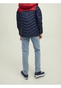 Marinblå och röd vinterjacka med chevronmönster; ljusblå jeans; mörka sneakers; sedd bakifrån som visar hela outfiten.