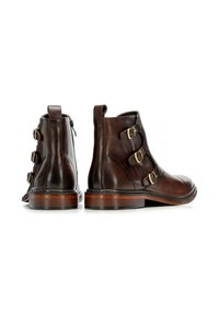 Botas de tobillo de cuero marrón con tres hebillas decorativas, puntera ligeramente redondeada y un sólido tacón de madera. Textura suave con detalles de costura.
