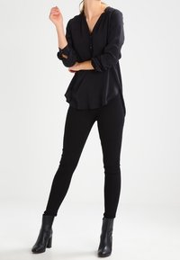 Svart button-up skjorta med långa ärmar; kombinerad med slim-fit svarta byxor och ankelboots; slät textur och avslappnad passform.