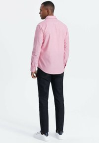 Vaaleanpunainen nappikauluksellinen paita pitkillä hihoilla, takanäkymä, yhdistettynä tummiin farkkuihin ja valkoisiin tennareihin neutraalilla taustalla.